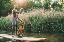 a man with his dog on a paddle board 