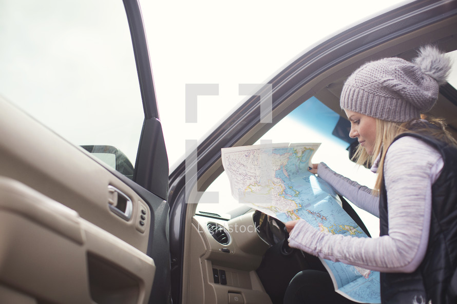 A woman looks at a map while sitting in a car.