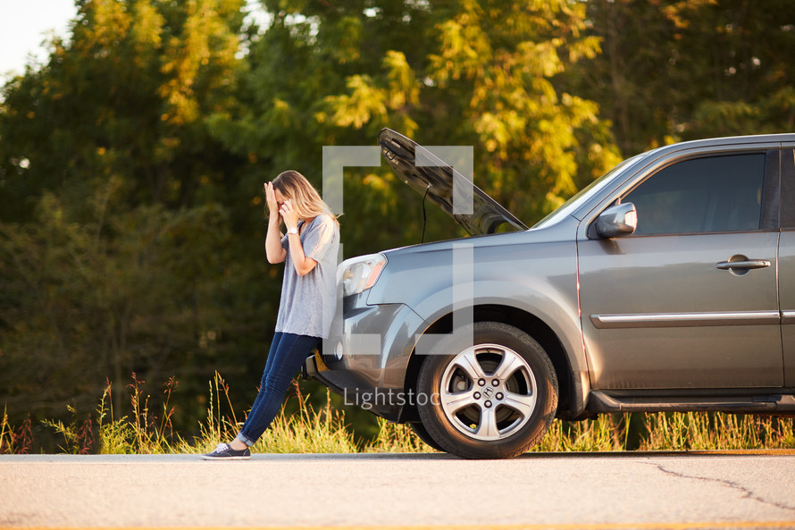 woman standing next to a vehicle broken down on the side of the road 