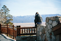 Woman sitting on a rock wall looking at the mountains