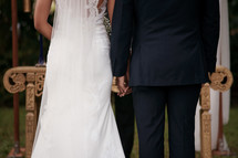 Photograph of a bride and groom exchanging vows, holding hands in front of pastor.