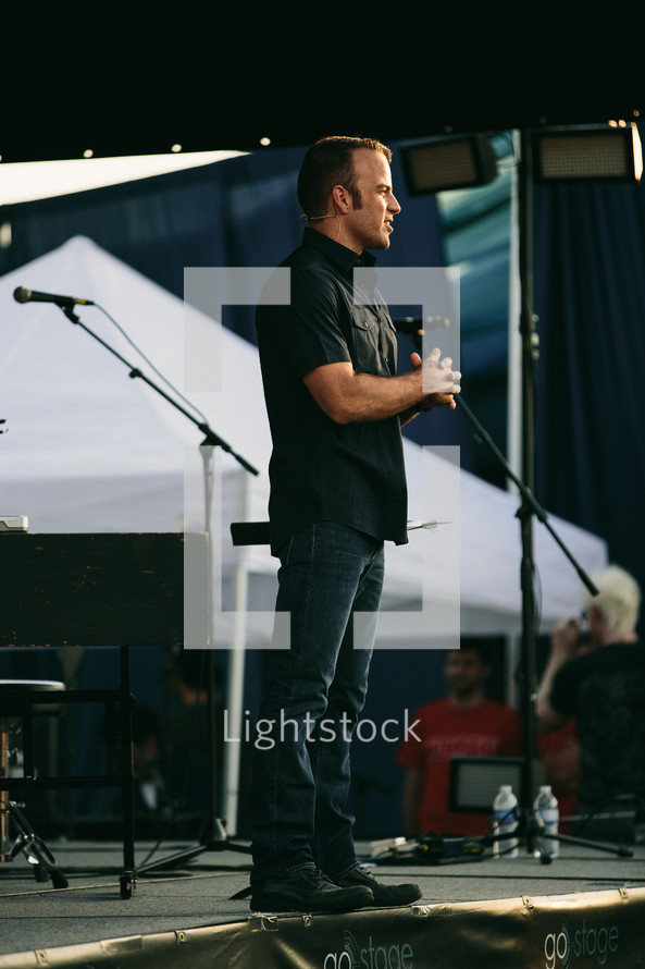 man at a microphone on stage at an outdoor worship service 