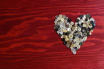 many little buttons shaping a heart on a red wooden background