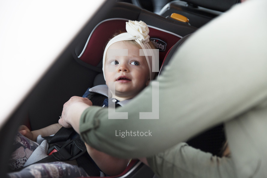 a mother fastening her toddler daughter into her carseat 
