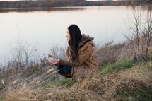 a woman squatting near a lake shore 