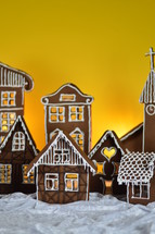 home made gingerbread village in front of yellow background on white snowlike velvet as advent decoration