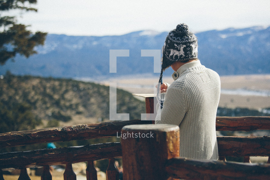 Man standing at a rail of a building looking out over the hills and mountains