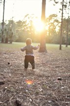 a toddler boy running in pine straw 
