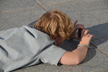 a boy lying on the ground taking a picture with a camera 