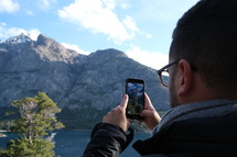 a man taking a picture of a mountain with his smartphone 