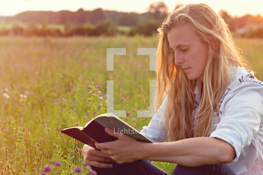 woman reading a Bible in a field of wildflowers 