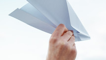 Hand of a girl is flying with a paper plane on the beach near the ocean