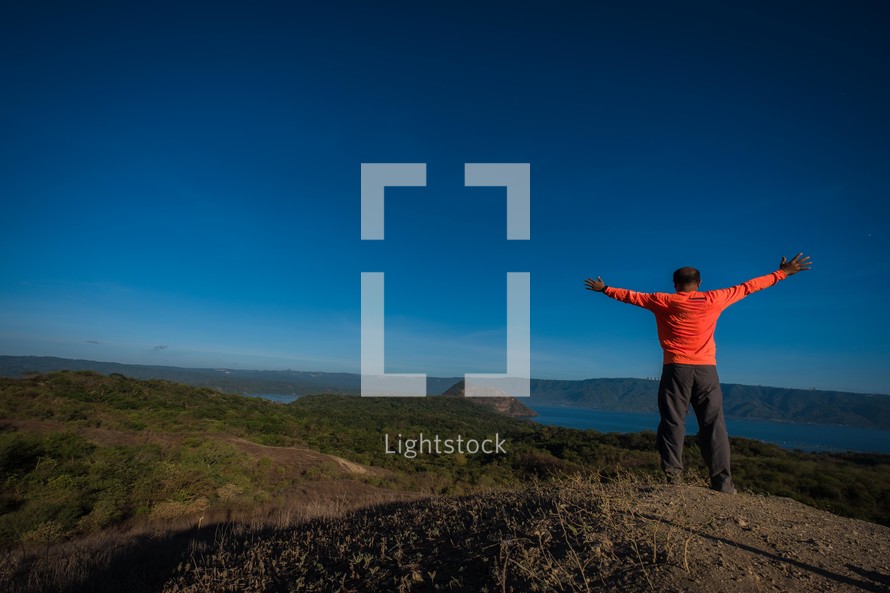 man with outstretched arms standing on a mountaintop 