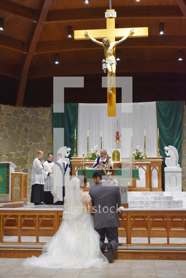 bride and groom kneeling in front of an alter to receive the eucharist  during their wedding 