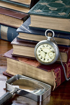 pocket watch, magnifying glass, and stacked books on a desk