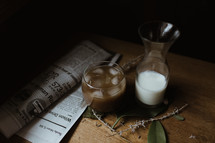 newspaper, creamer, coffee, and leaves on a wood table 