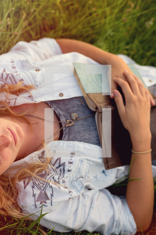 Woman laying in a field of grass holding a Bible.