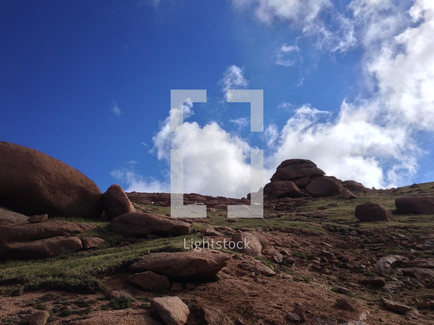 Boulders on a hillside with clouds in the blue sky.