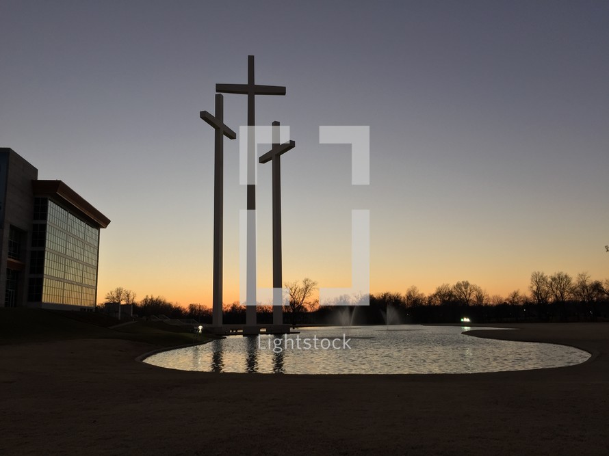 crosses in front of a pond near a church 