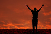 Silhouette of a man with arms raised praising God against and orange sky.