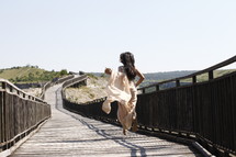 A woman in a long dress running down a boardwalk.