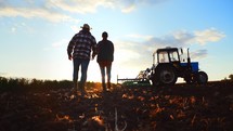 Silhouette couple walking through rural suburban area of field. Economic production with help of tractor machinery. Beautiful landscape nature. Suburban area with farm land. Healthy natural products.