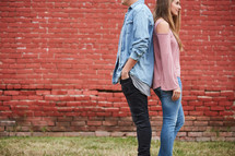 a couple standing back to back in front of a red brick wall 