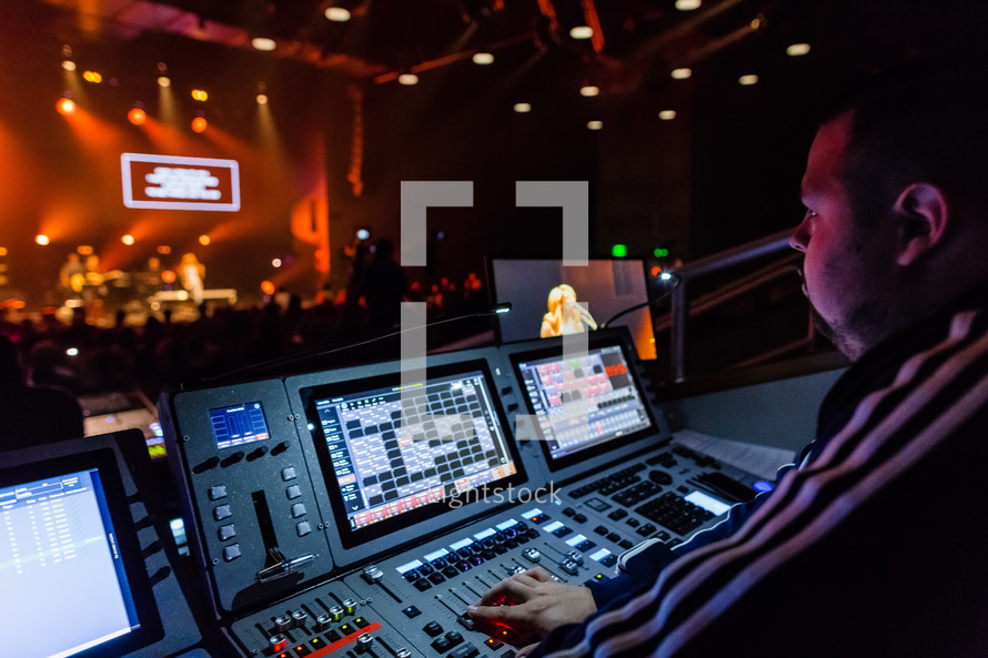 a man controlling the lights and sound behind a soundboard at a concert 