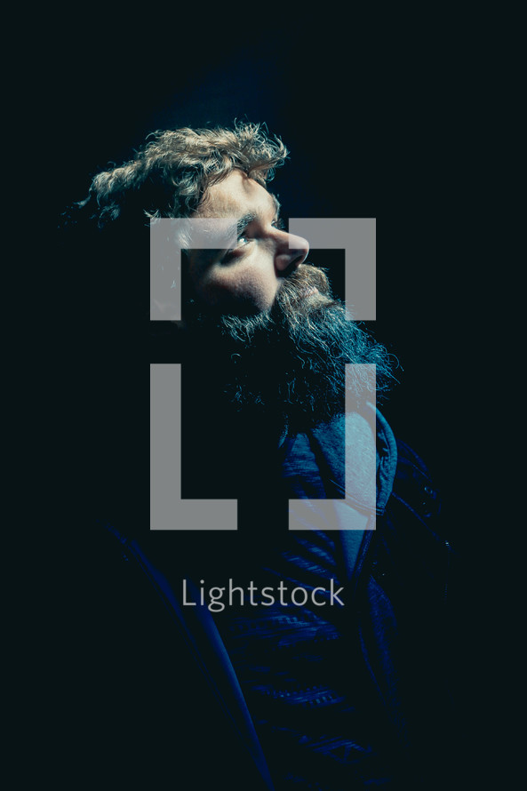 man with a thick beard looking up in darkness