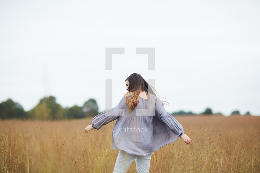 a young woman walking through a field with outstretched arms 