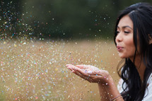 young woman blowing confetti out of her hands in a field 