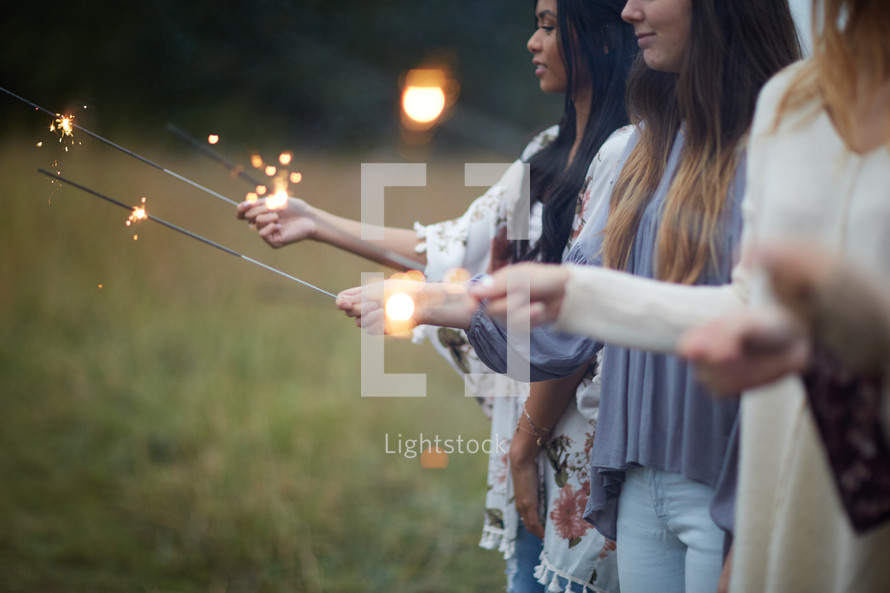 group of young women holding sparklers in a field  