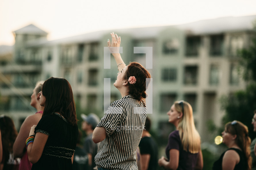 woman with her hand raised at an outdoor worship service 