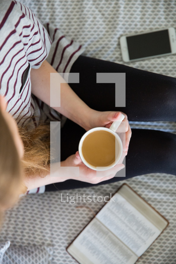 girl sitting on a bed with coffee, reading a Bible