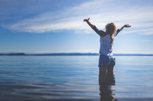 a woman wading in water with arms raised 