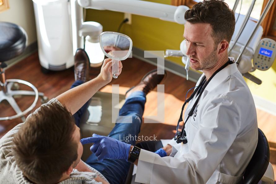 a dentist holding up a mirror for his patient to look at his teeth 