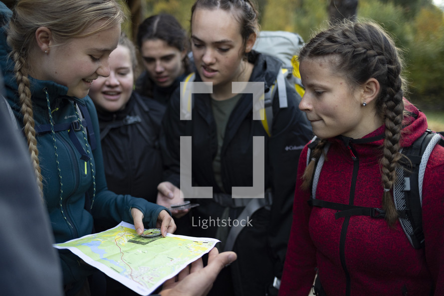 People in backpacks and outdoor clothing huddled around a trail map holding a compass 