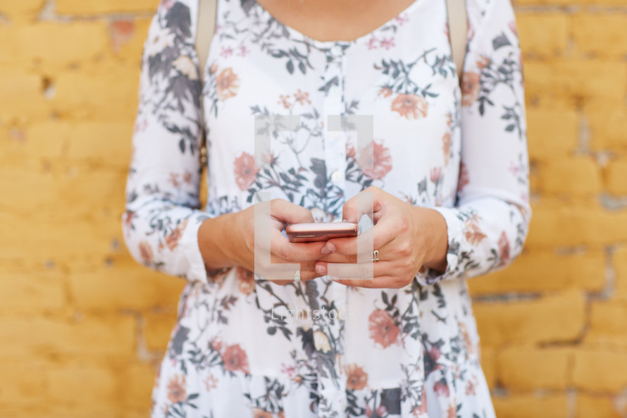 a woman standing in front of a yellow brick wall texting 
