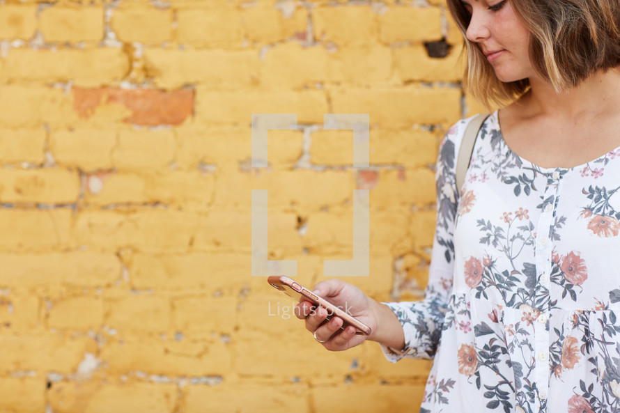 a woman standing in front of a yellow brick wall texting 