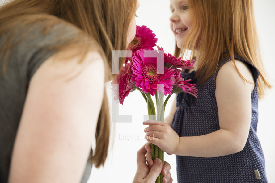 A little girl gives her mother a bouquet of pink flowers.