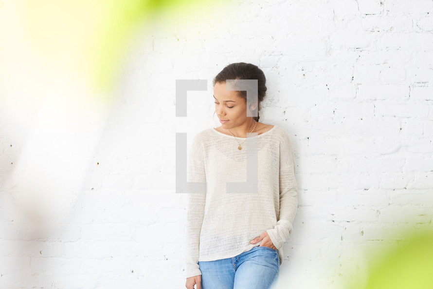 a woman leaning against a white brick wall 