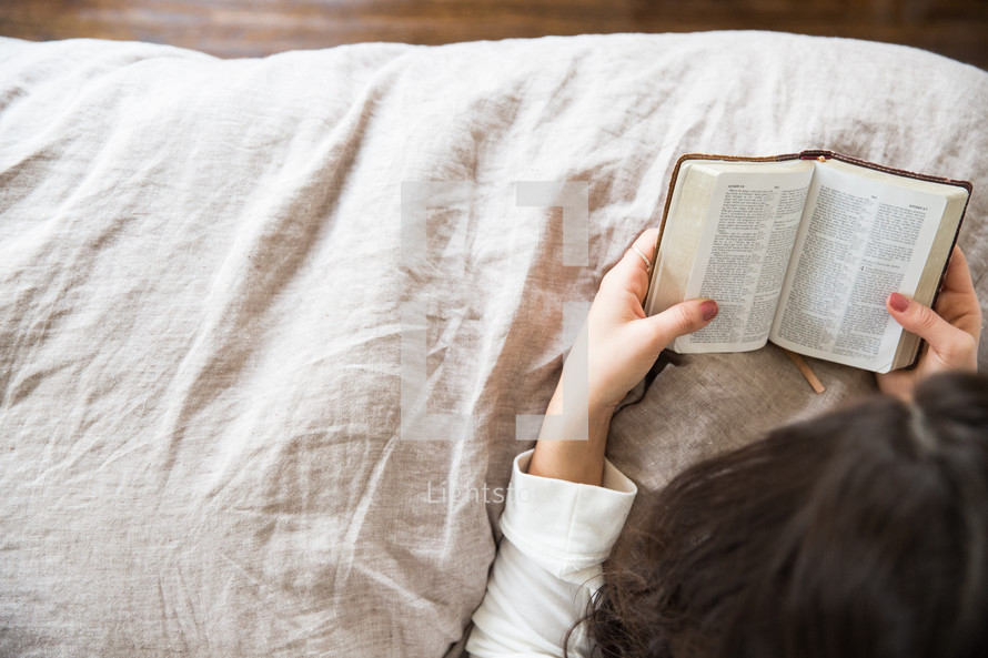 young woman reading a Bible in her bed