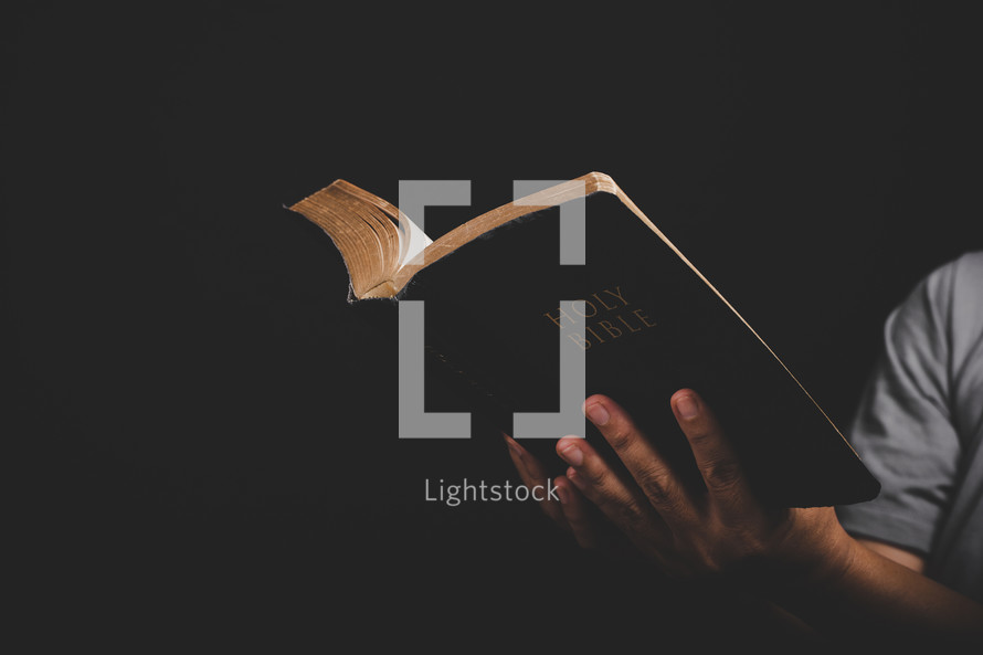 Hands holding up a Bible on a black background