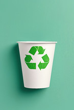 White paper cup with a green recycling symbol printed on it, placed against a light green background, representing eco-friendly practices and recycling.