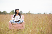 a young woman sitting in a chair in a field