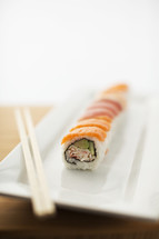 Sushi roll and chopsticks on a white plate.