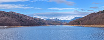 Mountain lake panorama against cloudy sky and mountains covered with snow