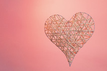A wooden, 3D heart with a pink background