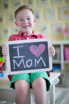 a little boy holding a chalkboard sign that reads I heart mom 