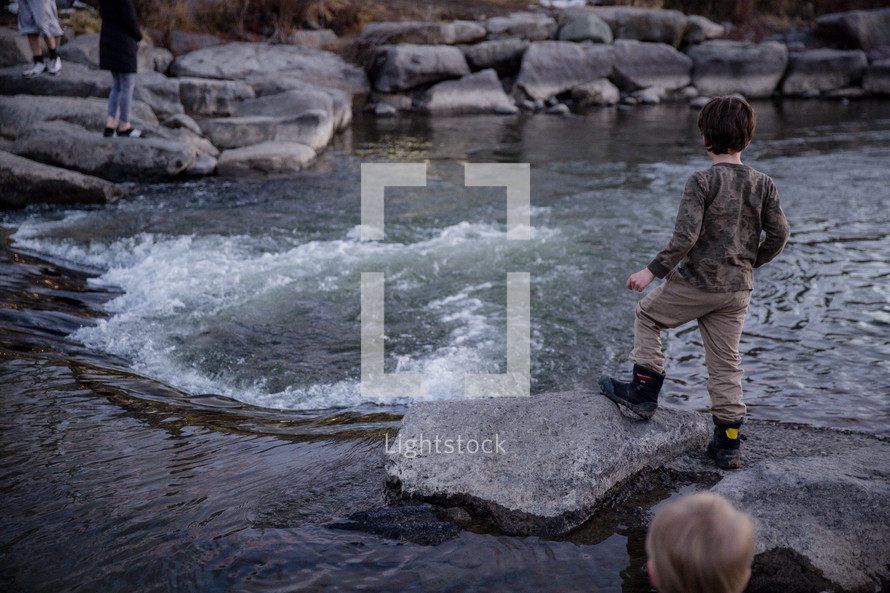 children standing on rocks along a riverbank 